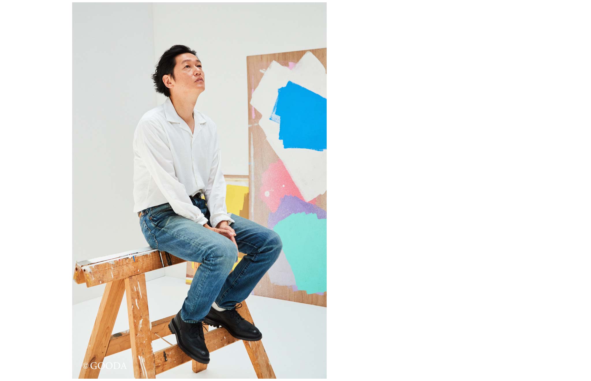白シャツにユーズド加工のジーンズ姿で木の台に座る俳優の井浦新
